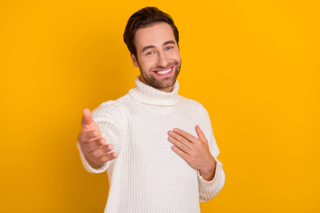 Foto van grappige aantrekkelijke man dragen witte trui geven u arm geïsoleerde gele kleur achtergrond. - Foto, afbeelding