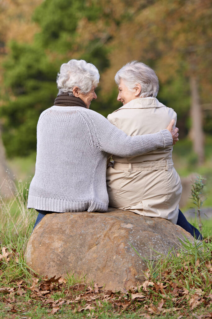 Миттєво роздумуючи над життям. Вид ззаду на двох старших жінок, які сидять на скелі разом
 - Фото, зображення