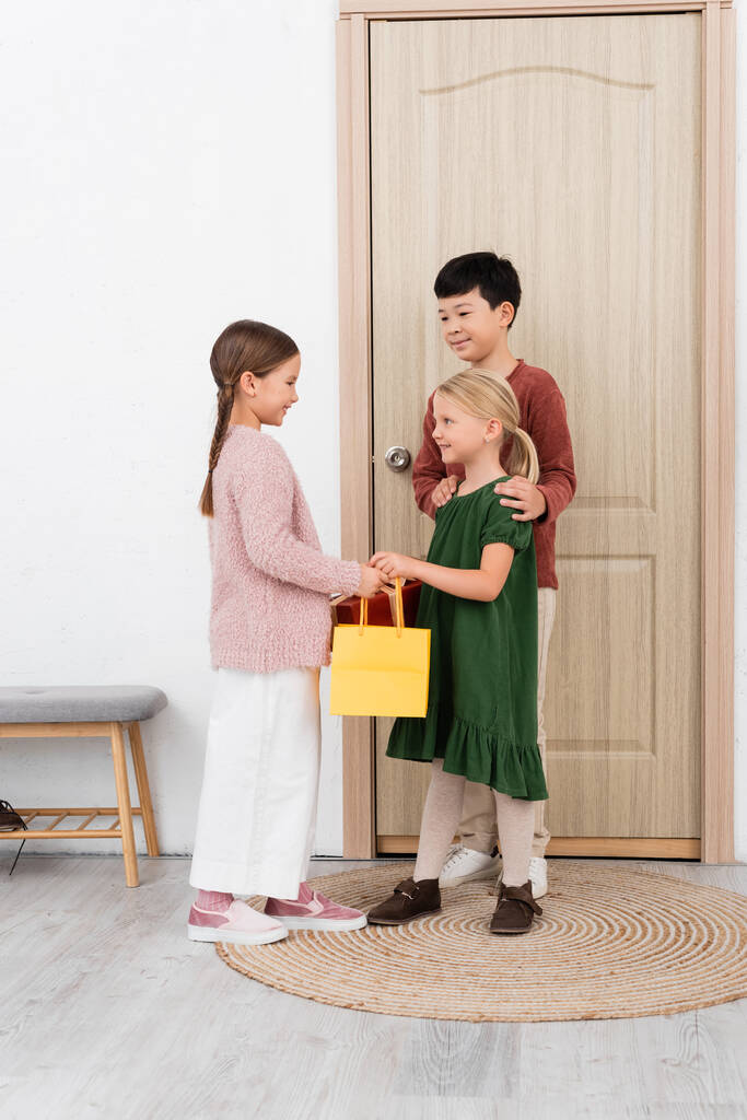 Interraciale kinderen geven boodschappentas en cadeau aan vriend thuis  - Foto, afbeelding