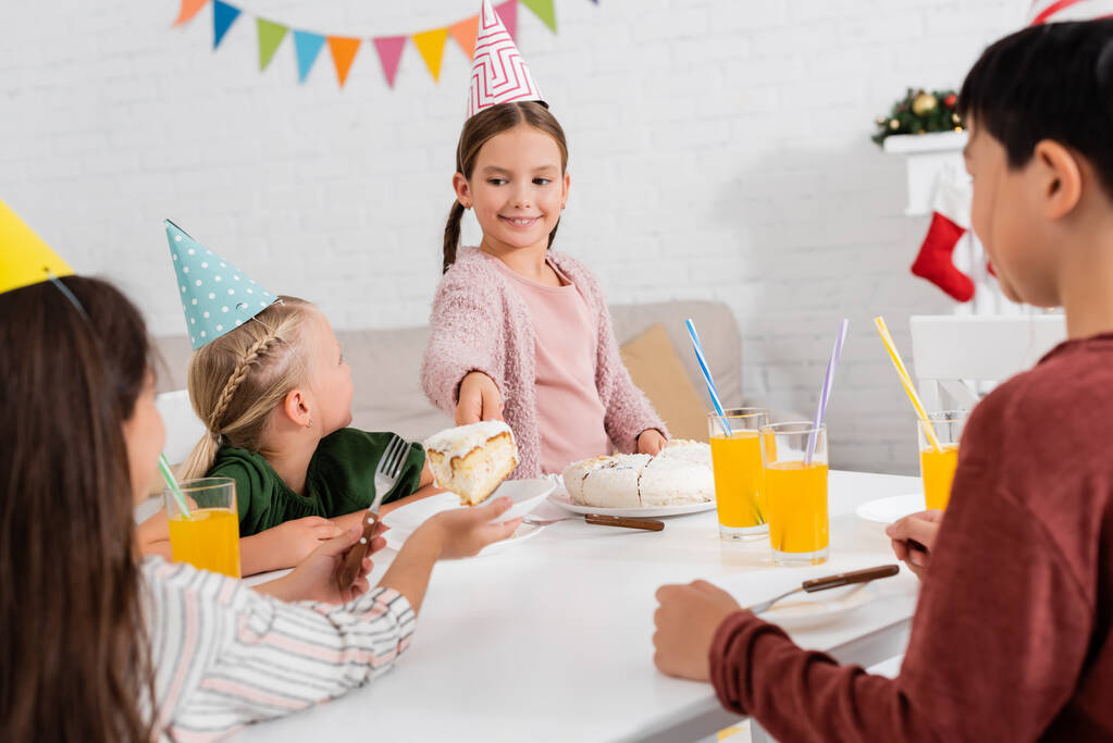 Vidám gyerek fél sapkában, szülinapi tortát ad a barátjának az otthoni ünneplés alatt.  - Fotó, kép
