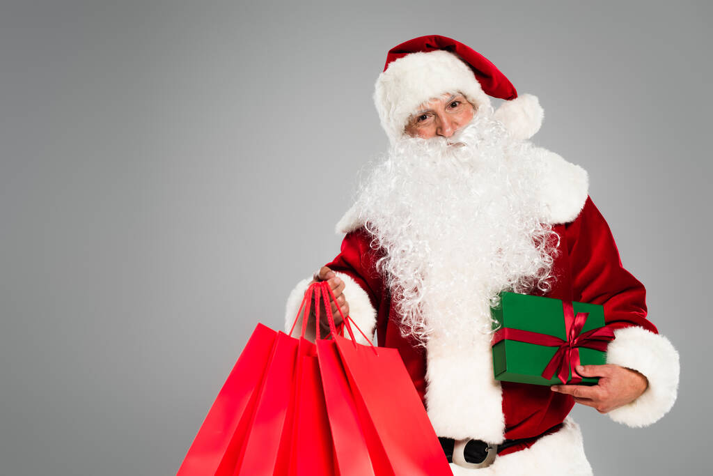 Санта-Клаус тримає подарунок і сумки для покупок ізольовані на сірому
  - Фото, зображення