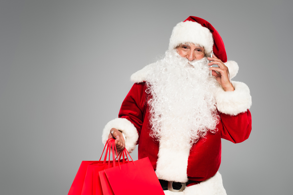 Joulupukki puhuu älypuhelimella ja pitää ostoskassit eristetty harmaa  - Valokuva, kuva
