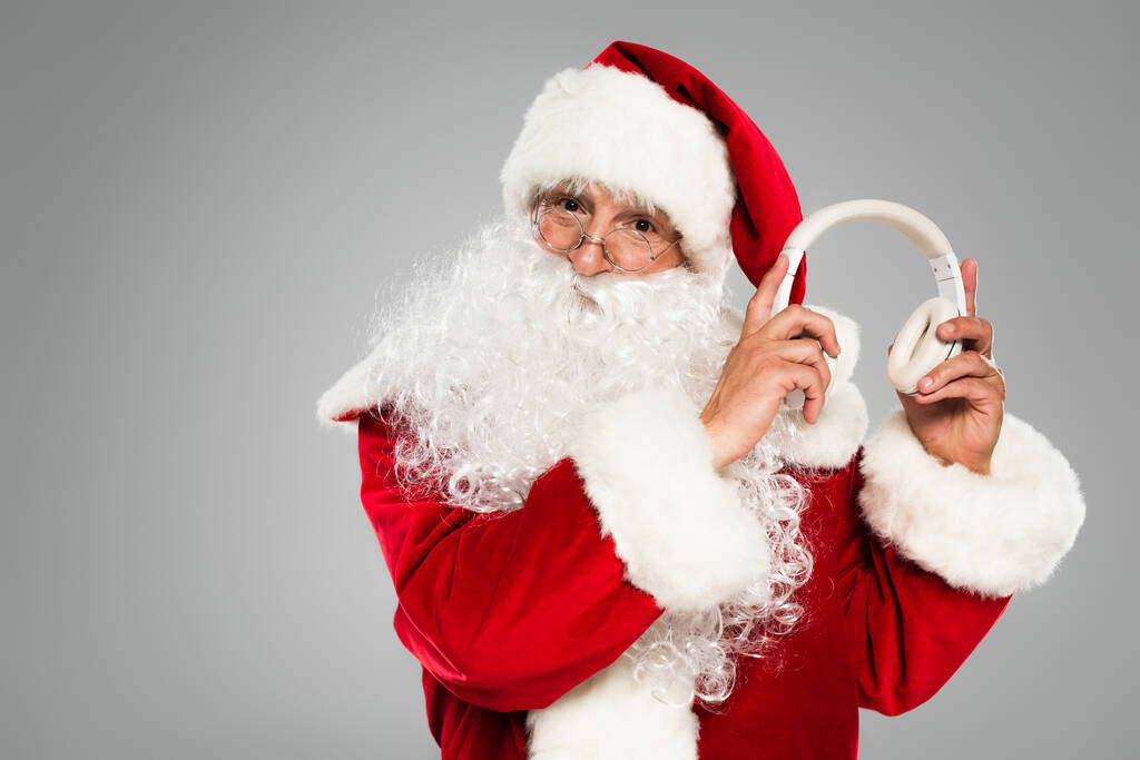 Санта-Клаус в очках с наушниками, изолированными на сером  - Фото, изображение