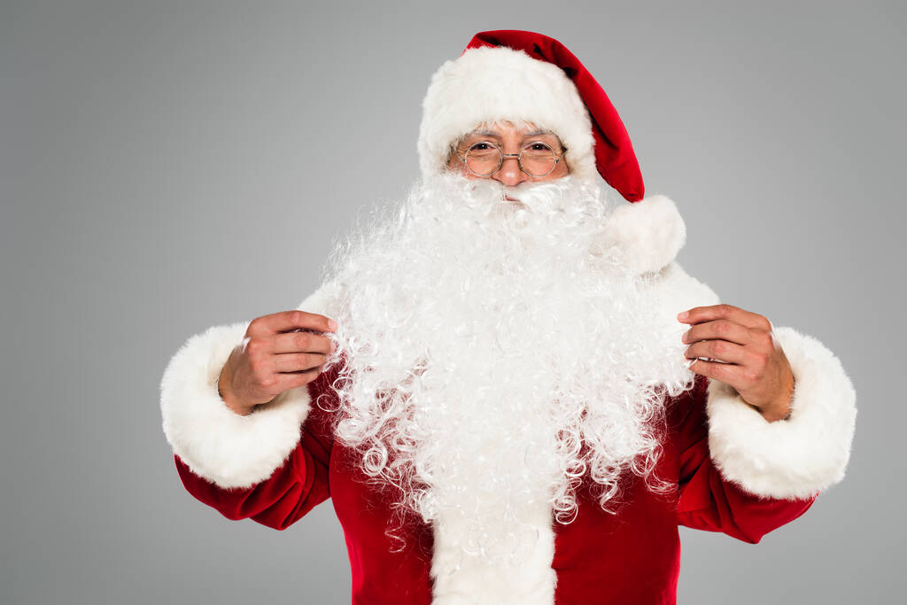 Kerstman in bril en hoed kijkend naar camera geïsoleerd op grijs  - Foto, afbeelding