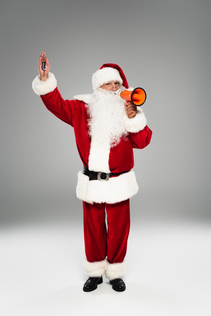 Plná délka Santa Claus drží klíček od auta a reproduktor na šedém pozadí  - Fotografie, Obrázek