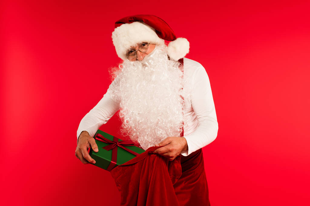 Apa karácsony kalapban tesz ajándékot zsákba elszigetelt piros  - Fotó, kép