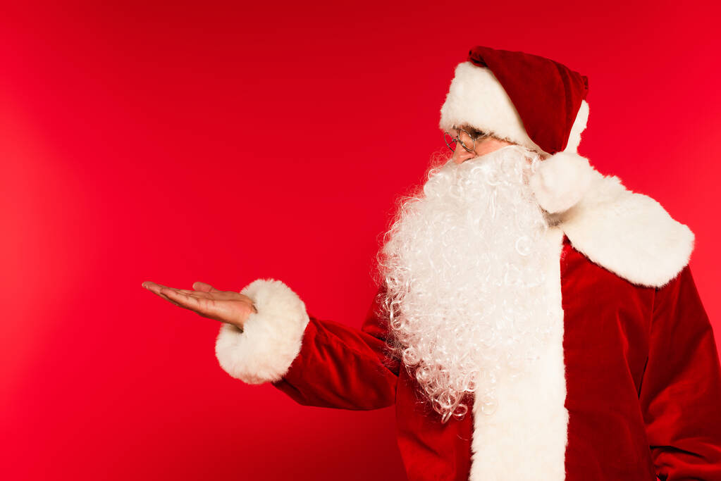 Бородатый Санта Клаус указывает рукой на красный фон  - Фото, изображение