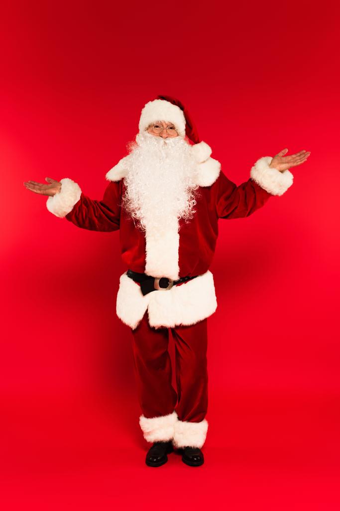 Weihnachtsmann im Kostüm zeigt mit den Händen auf rotem Hintergrund  - Foto, Bild