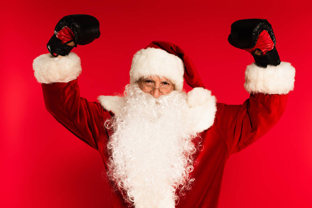 Babbo Natale in costume e guanti da boxe che mostrano i muscoli su sfondo rosso  - Foto, immagini