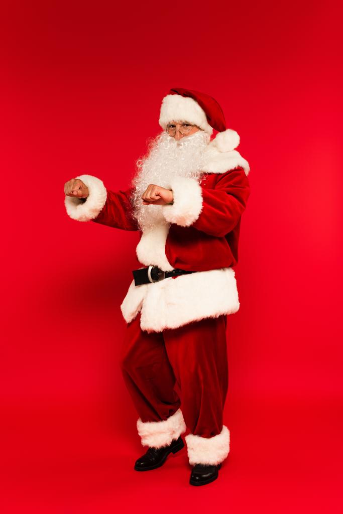 Babbo Natale barbuto guardando la fotocamera mentre ballava su sfondo rosso  - Foto, immagini