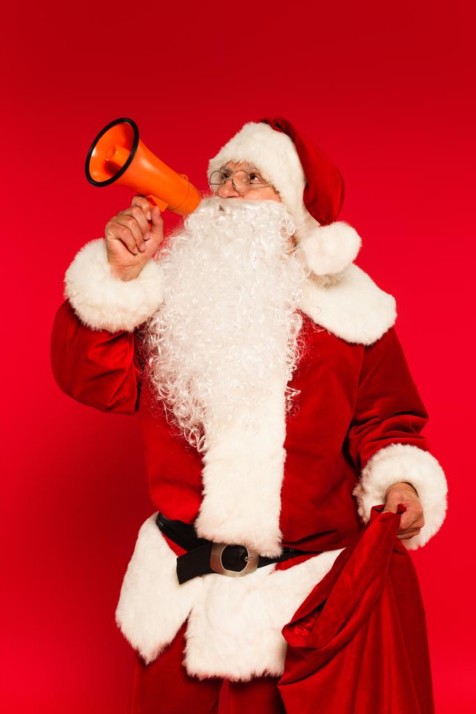 Weihnachtsmann hält Lautsprecher und Sack auf rotem Hintergrund  - Foto, Bild