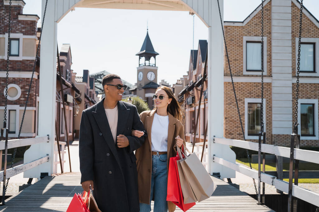 elegante e feliz casal multiétnico com sacos de compras na ponte da cidade - Foto, Imagem