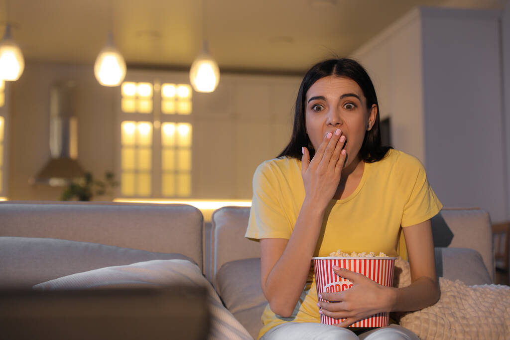 Young woman watching movie with popcorn on sofa at night, space for text - Photo, Image