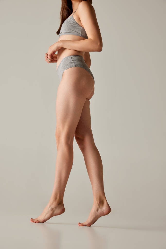Oříznutý obraz štíhlého a sportovního ženského těla ve spodním prádle, hladké nohy izolované přes šedé pozadí studia. Pojetí krásy, péče o tělo a pokožku, zdraví, plastická chirurgie, kosmetika, sport - Fotografie, Obrázek