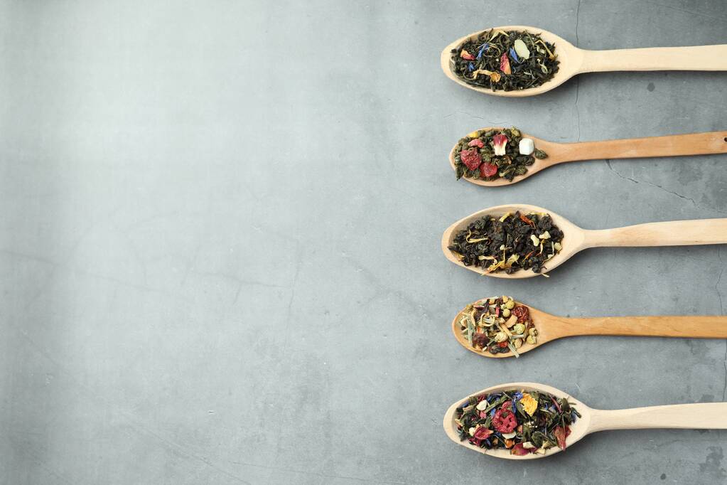 Diferentes tipos de té de hierbas secas en cucharas de madera en la mesa gris claro, la puesta plana. Espacio para texto - Foto, Imagen