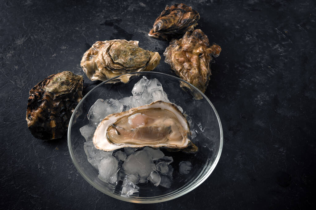 Open oester op gemalen ijs op een glasplaat en gesloten oesters op een donkere rustieke achtergrond, kopieerruimte, bovenaanzicht van boven geselecteerde focus - Foto, afbeelding