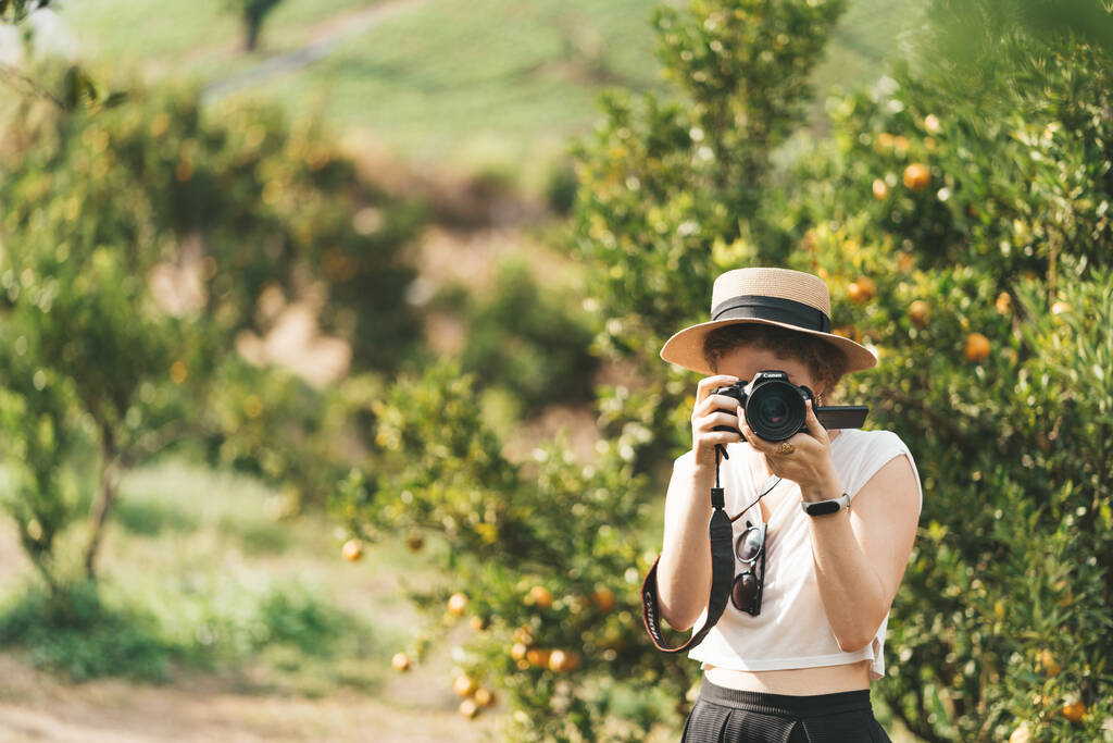 藁帽子の女性がオレンジの庭で写真を撮っています。高品質の写真 - 写真・画像
