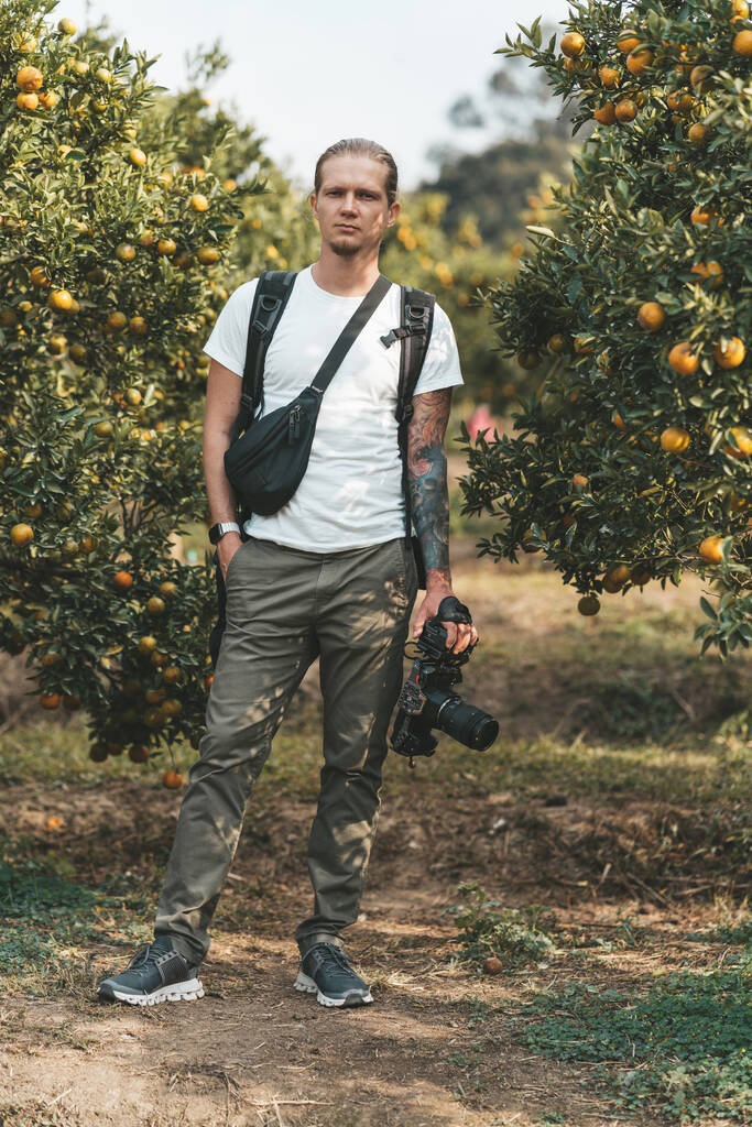 Kamerzysta stojący w pomarańczowym ogrodzie z kamerą wideo - Zdjęcie, obraz