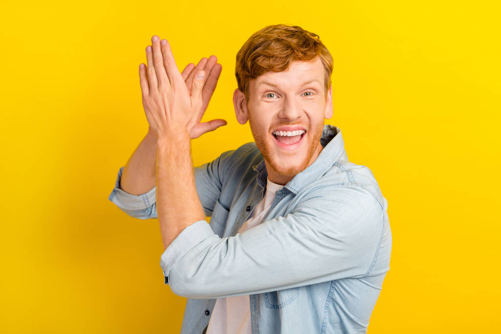 Фото веселого позитивного чоловіка в джинсовій сорочці, що плескає руками, посміхаючись ізольованому жовтому кольоровому фоні
. - Фото, зображення