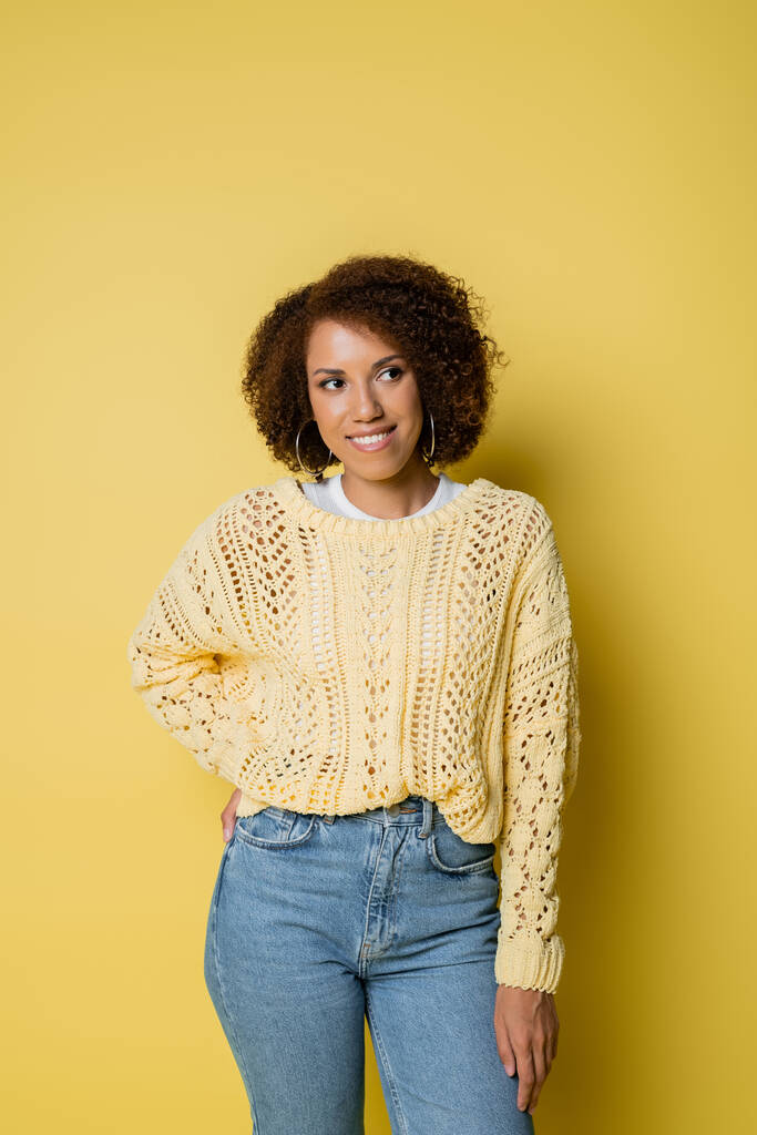 šťastná a mladá africká americká žena v pleteném svetru s úsměvem na žluté - Fotografie, Obrázek