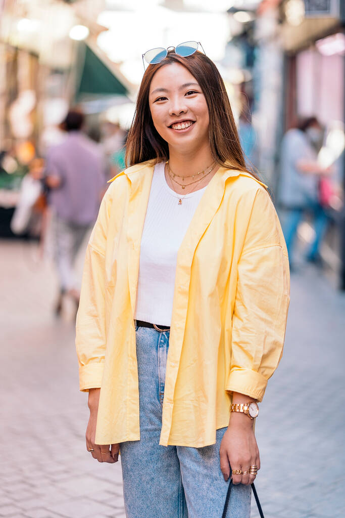 Coole Asiatin in lässiger Kleidung, die in der Stadt in die Kamera lächelt. - Foto, Bild