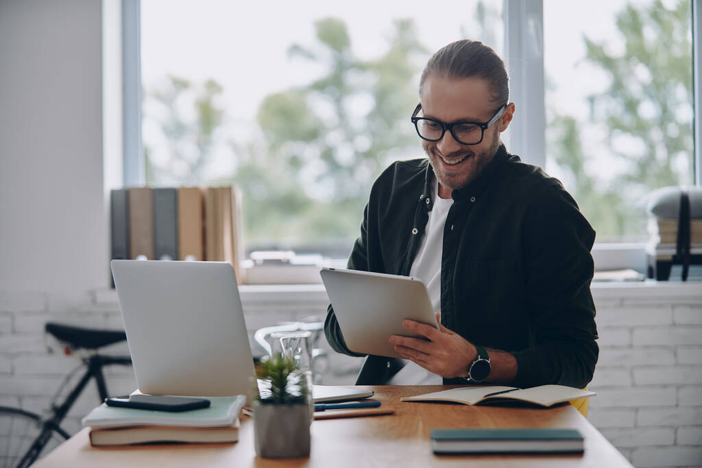 Fröhlicher junger Mann mit digitalem Tablet am Arbeitsplatz im Büro - Foto, Bild