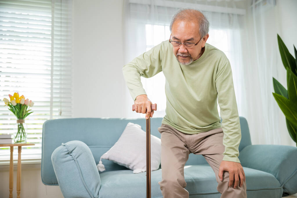Azjatycki starszy starzec w okularach typu do wstawania z sofy z laską chodzącą kijem chodzić w domu, Starszy cierpi na ból kolana trzymając uchwyt trzciny, emerytury opieki medycznej - Zdjęcie, obraz