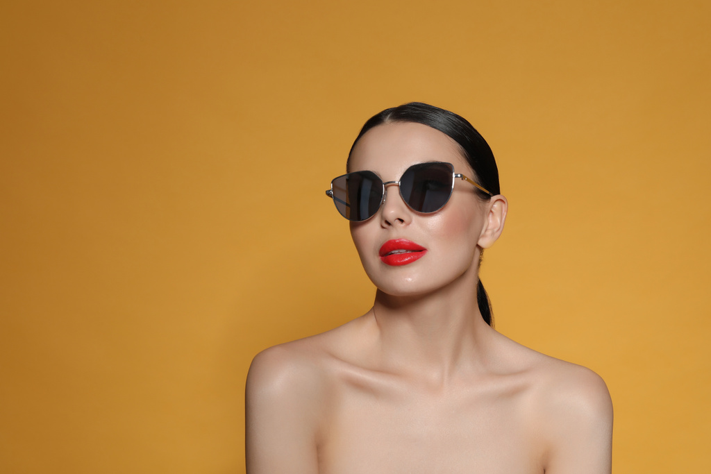 Привлекательная женщина в модных солнечных очках на оранжевом фоне. Пространство для текста - Фото, изображение