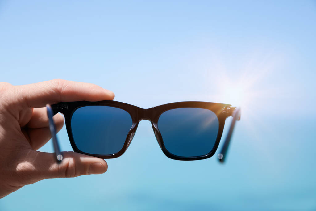 Starší muž drží stylové sluneční brýle proti modré obloze, detailní záběr - Fotografie, Obrázek