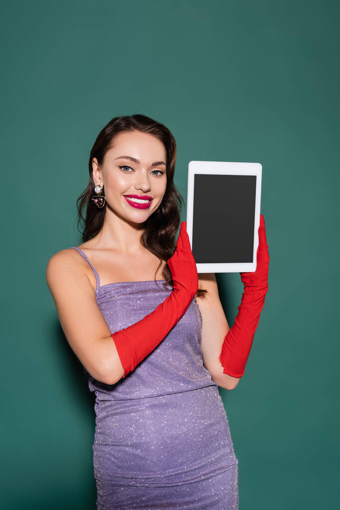 gelukkig jonge vrouw in paarse jurk en handschoenen houden digitale tablet met leeg scherm op groen - Foto, afbeelding