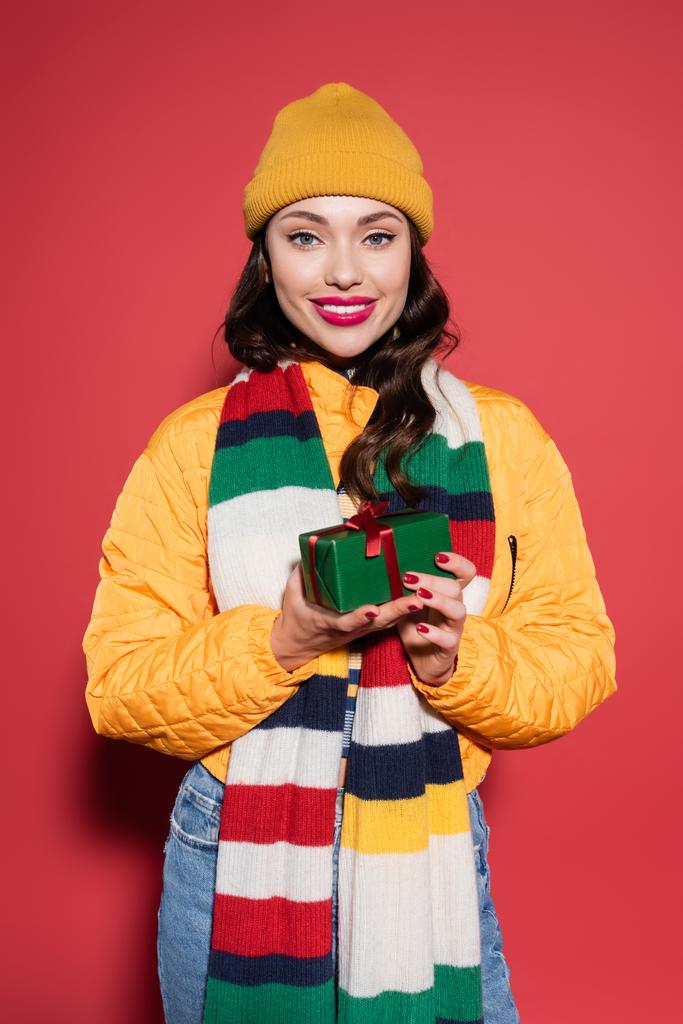mulher feliz em chapéu gorro e cachecol segurando embrulhado caixa de presente em vermelho - Foto, Imagem