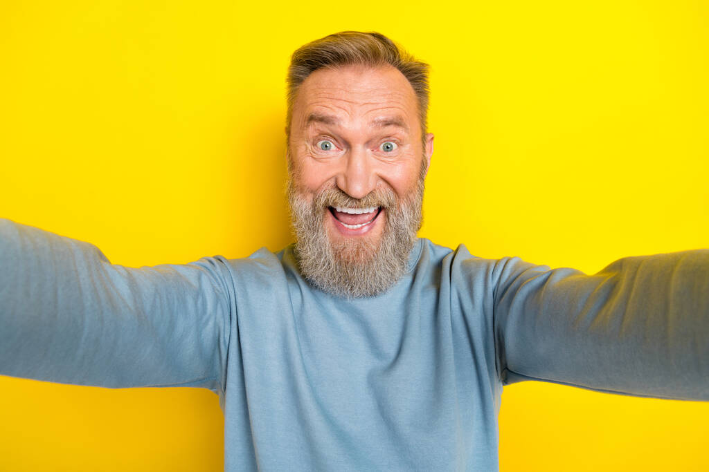 Fénykép jóképű izgatott férfi nyugdíjas öltözött kék pulóver felvétel self video izolált sárga szín háttér. - Fotó, kép