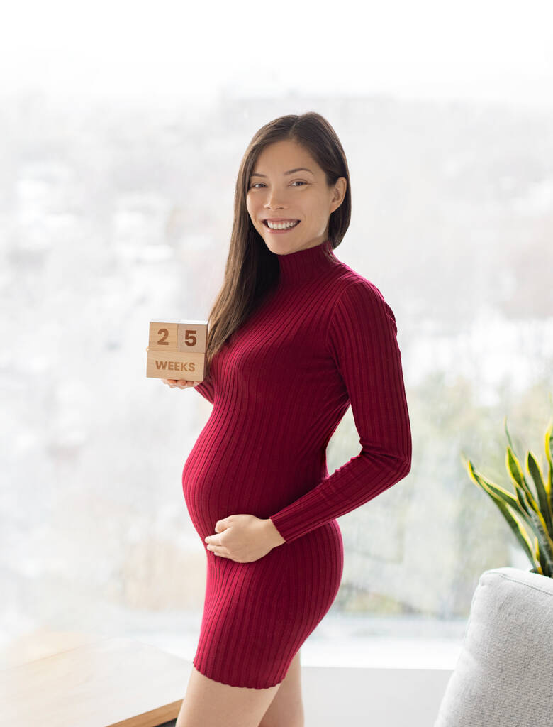 Asian pregnant woman showing 25 weeks pregnancy bump for maternity photoshoot holding wooden blocks sign happy. Vertical crop. - Photo, Image