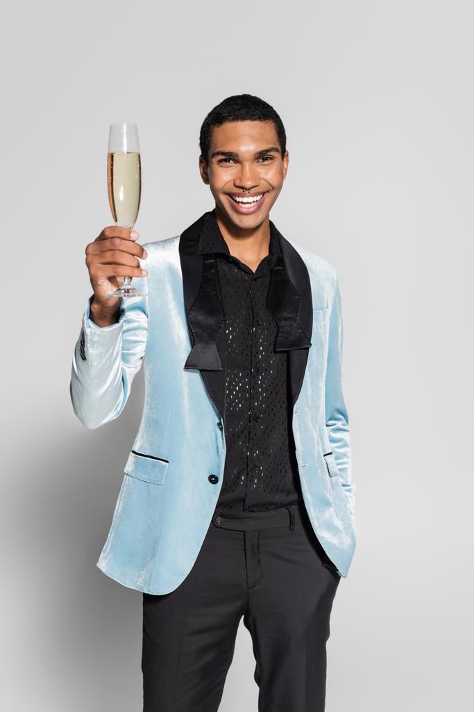 gelukkig Afrikaans amerikaanse man in elegante feestelijke kleding toasten met champagne geïsoleerd op grijs - Foto, afbeelding