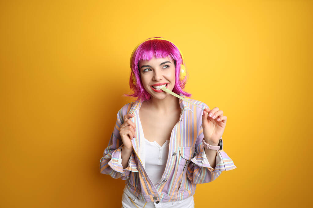 Mulher nova na moda em peruca colorida com fones de ouvido mastigar bubblegum no fundo amarelo - Foto, Imagem