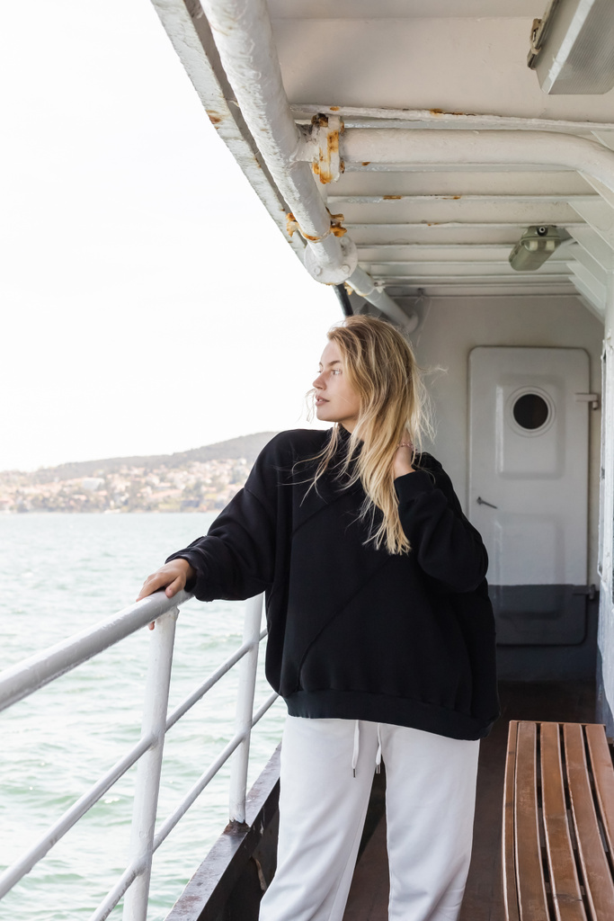 blonde vrouw in zwarte trui kijken naar zee vanaf veerboot kruising bosporus in Istanbul  - Foto, afbeelding