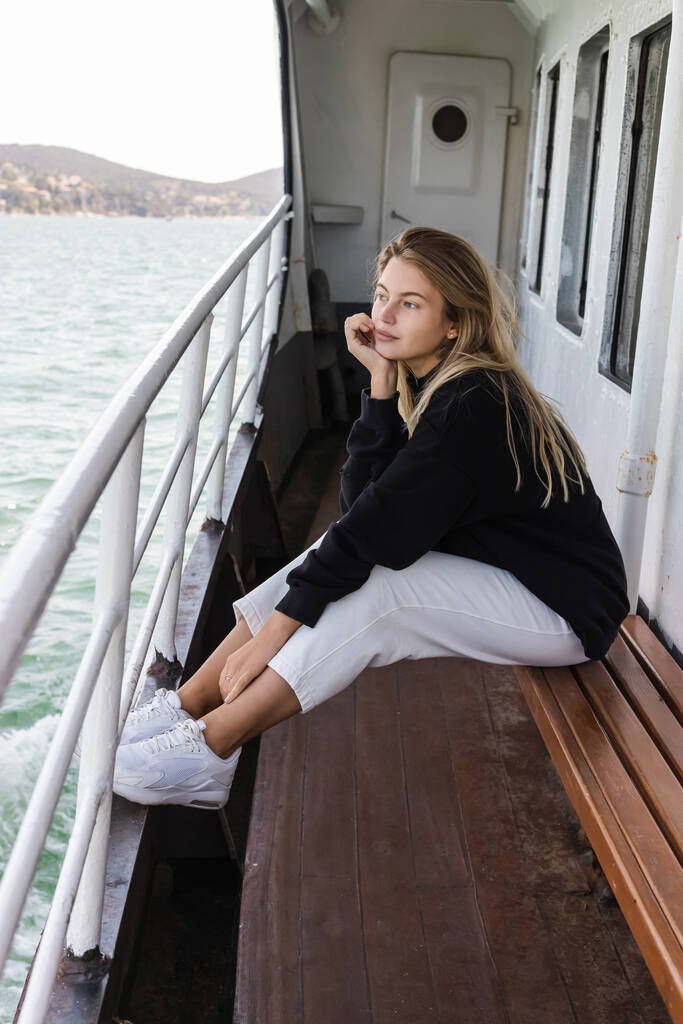 夢のような黒のセーターを着た女性がベンチに座りながら渡し船から海を眺め - 写真・画像