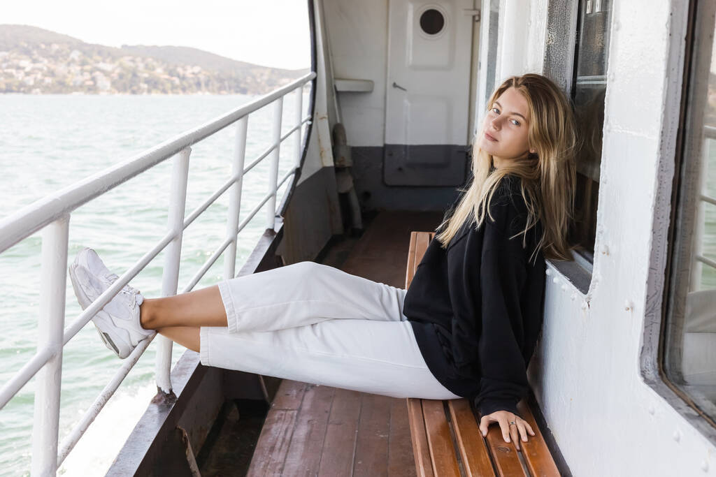Блондинка в чорному светрі сидить на лавці в поромному човні, перетинаючи Босфор у Істанбулі.  - Фото, зображення