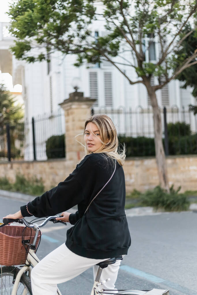 jeune femme blonde en tenue de vélo à la mode et regardant la caméra dans la rue en dinde - Photo, image