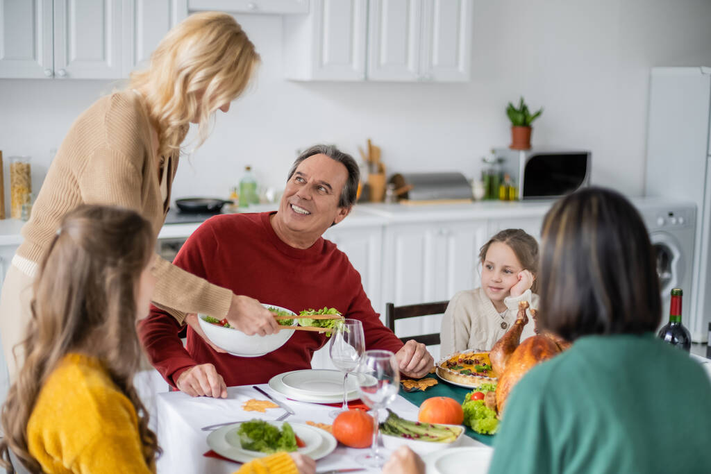 Donna che tiene l'insalata vicino a genitori e figlia durante la cena del Ringraziamento a casa  - Foto, immagini