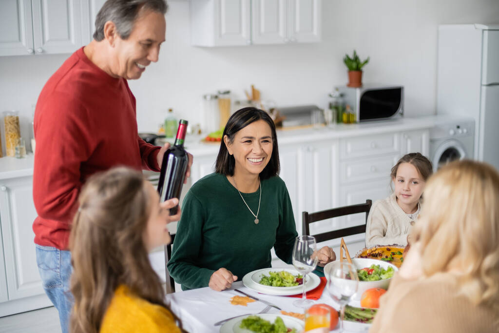 Многонациональная женщина сидит рядом с семьей и вкусный ужин День благодарения на кухне  - Фото, изображение