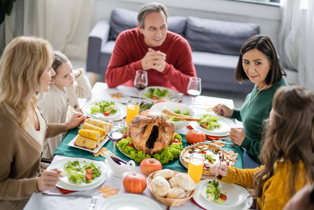 Família inter-racial conversando perto de saboroso jantar de ação de graças e bebidas em casa  - Foto, Imagem