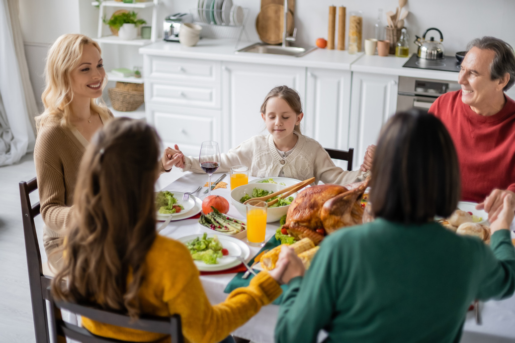 Hymyilevä perhe pitää toisiaan kädestä lähellä kiitospäivän illallista drinkkien kanssa kotona  - Valokuva, kuva