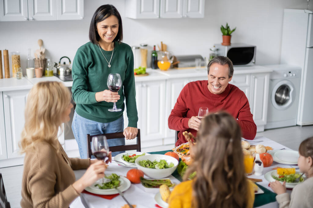 Monietninen nainen tilalla lasi viiniä lähellä hämärtynyt perhe ja kiitospäivä illallinen  - Valokuva, kuva