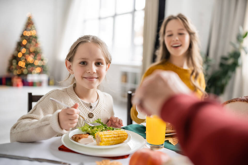 Улыбающийся ребенок смотрит в камеру рядом с праздничным ужином с семьей дома  - Фото, изображение