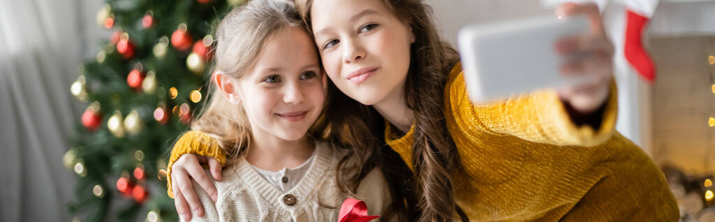 Dívka objímání sestra a brát selfie během nového roku doma, banner  - Fotografie, Obrázek