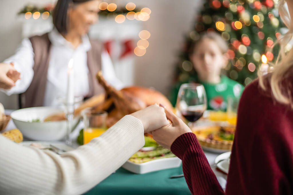 багатоетнічна сім'я тримає руки і молиться перед різдвяною вечерею на розмитому фоні
 - Фото, зображення