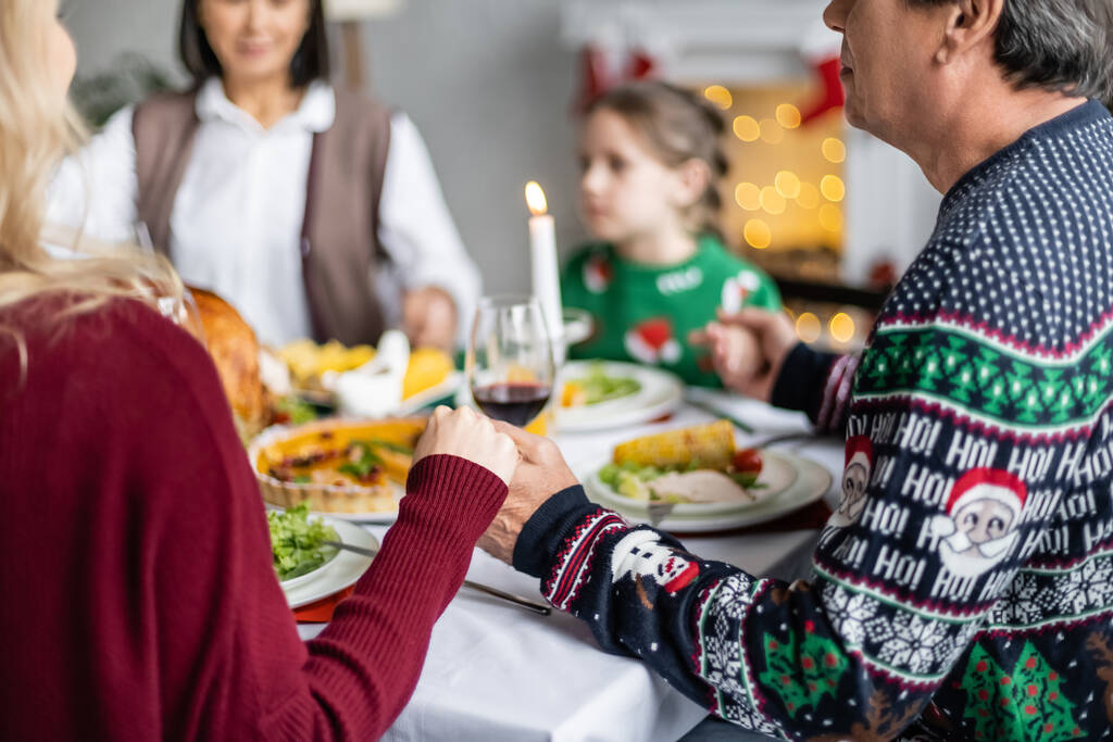 многонациональная семья, держась за руки и молясь возле праздничного ужина во время празднования Рождества - Фото, изображение