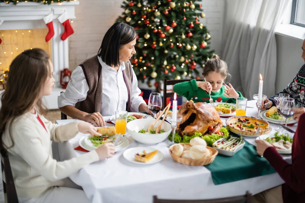 multiracial woman looking at granddaughter during christmas dinner with family - Photo, Image