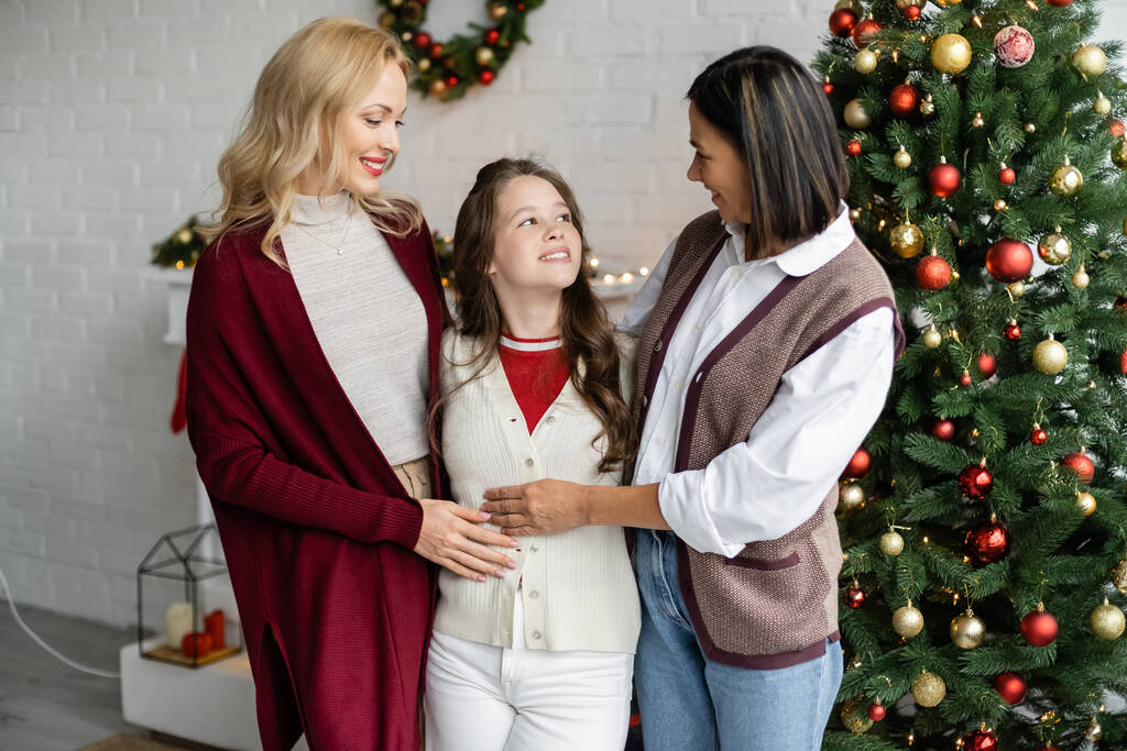 joyeuse adolescente souriant près de la mère et mamie multiraciale près de l'arbre de Noël - Photo, image